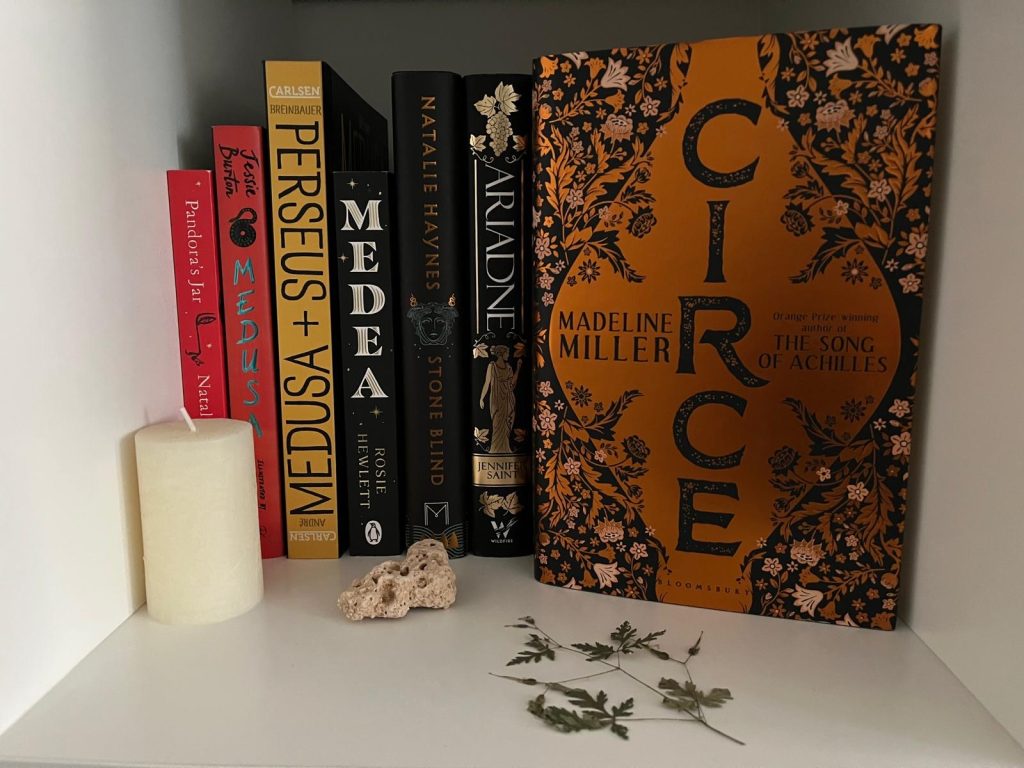 The book “Circe” by Madeline Miller on a shelf with a white candle and herbal decorations.