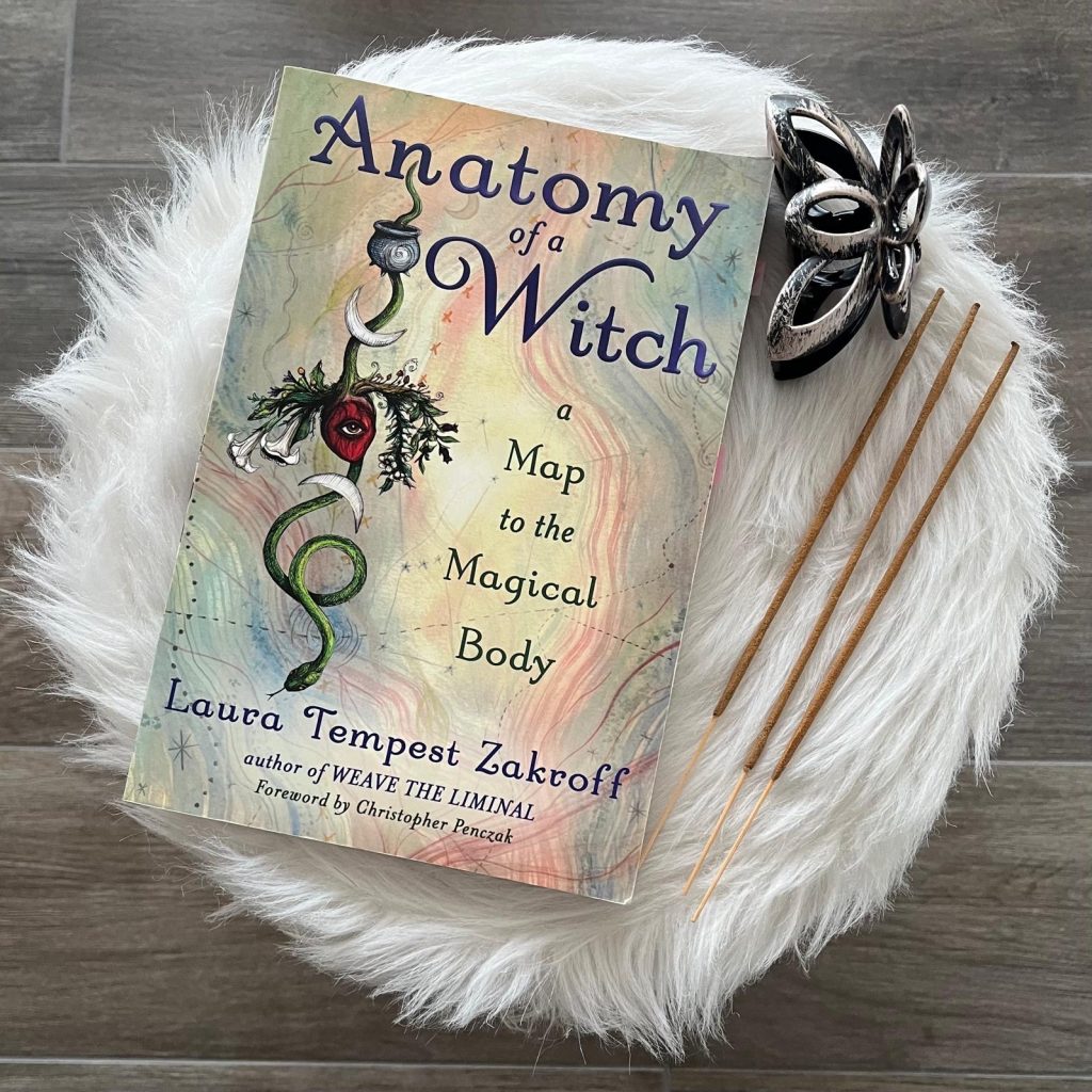 Das Buch Anatomy of a Witch: A Map to the Magical Body von Laura Tempest Zakroff auf weissem Fell mit Räucherstäbchen und silberner Dekoration.